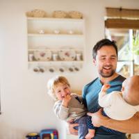 Father holding happy infant and toddler in brightly lit home