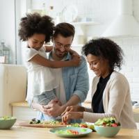 Happy, healthy parents preparing salad for lunch with young daughter