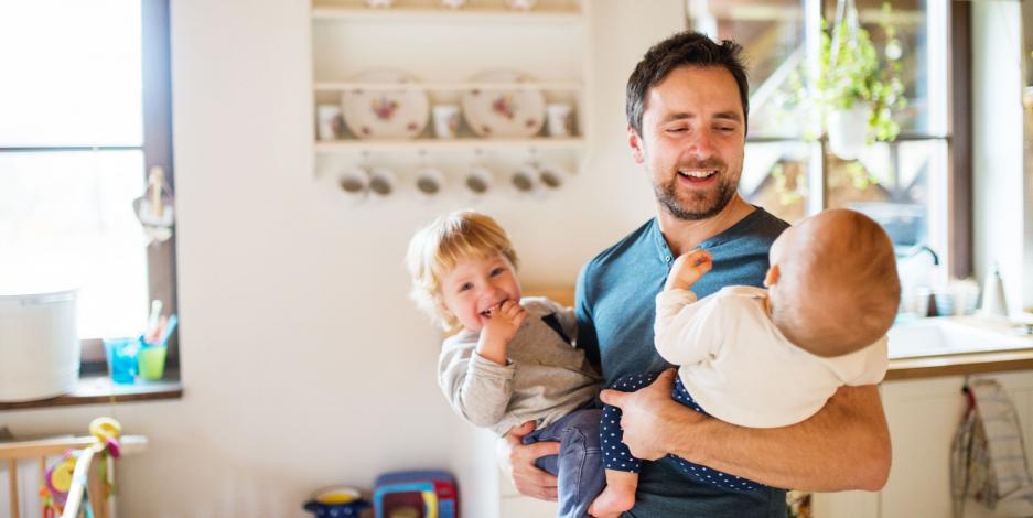 Father holding happy infant and toddler in brightly lit home