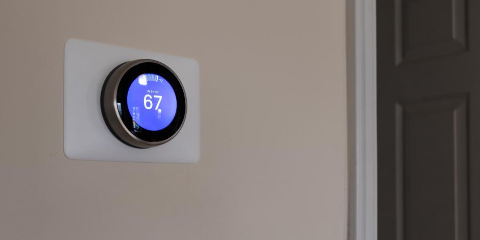 Smart thermostat on ecru wall to the left of wooden door Smart thermostat on ecru wall to the left of wooden door