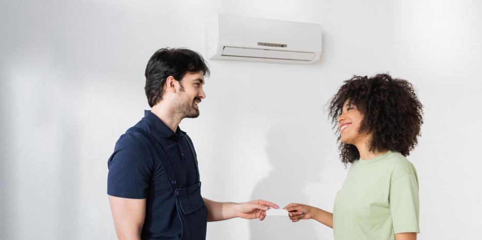 HVAC technician standing in front of mini split system on wall, talking with homeowner